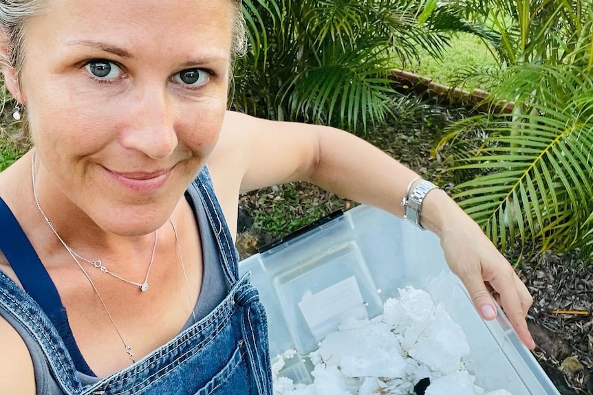 A white woman wearing denim overalls with a tub full of polystyrene