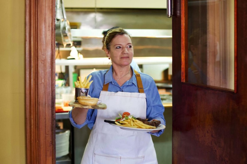 A woman carries plates of food out of a hotel kitchen.