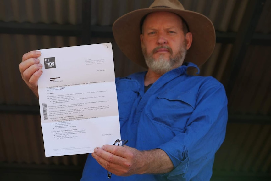 A photo of a man in a blue shirt and an akubra holding a letter out towards the camera.