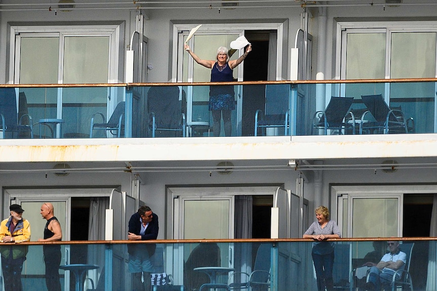 A passenger waves from the deck of a cruise ship.