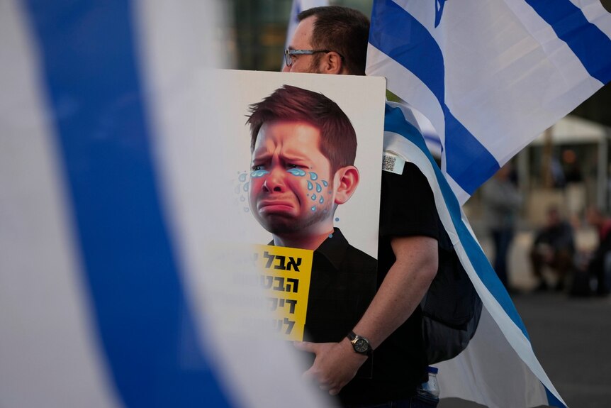 A man carries a poster with a picture of a young man with cartoon tears on it 