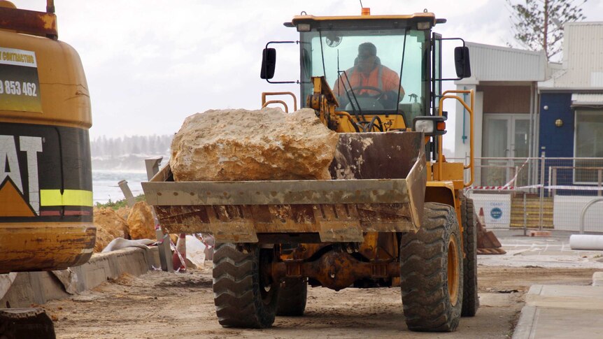 A tractor carrying a large rock being driven along a pathway on Port Beach