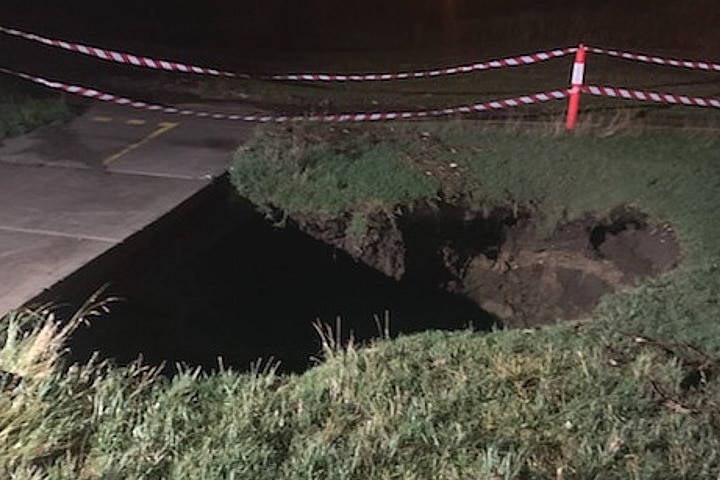 A sink hole at night with emergency tape around it as a barrier.