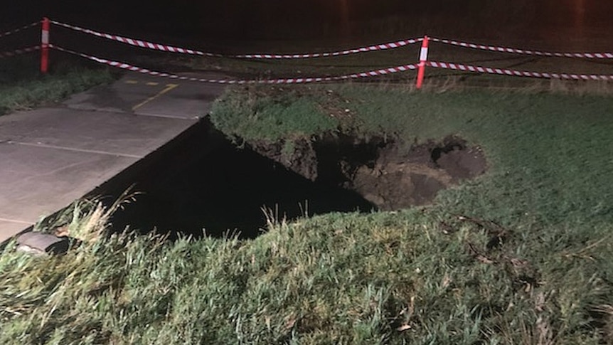A sink hole at night with emergency tape around it as a barrier.