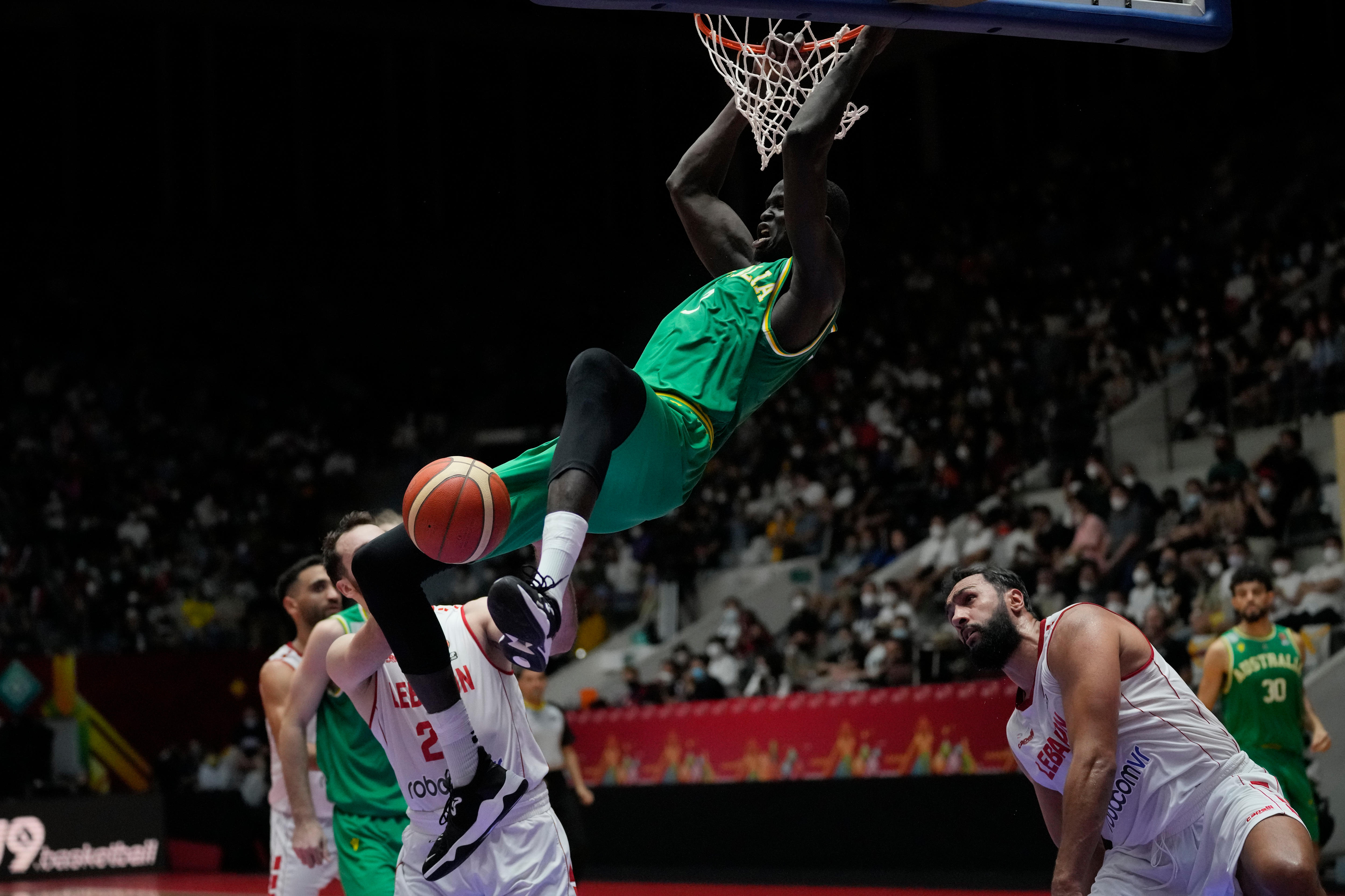 An Australian basketballer hangs off the rim after his dunk while a number of Lebanon players watch.