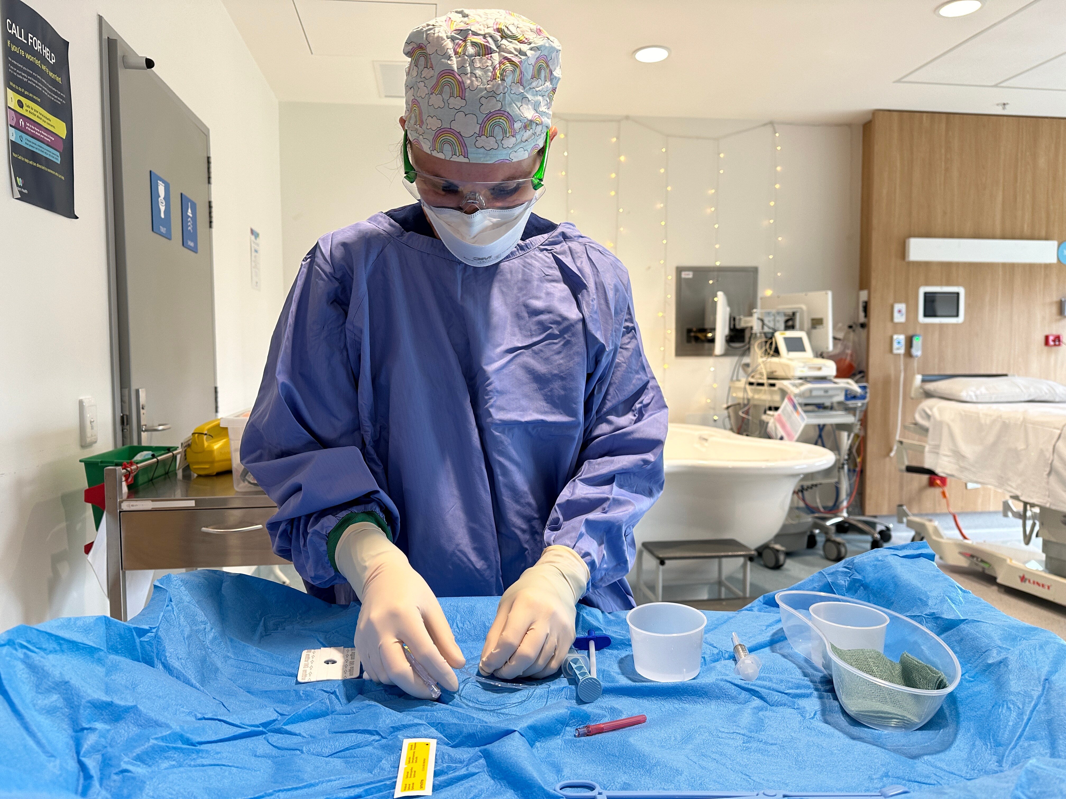 A nurse in medical scrubs and a mask is seen in a hospital room