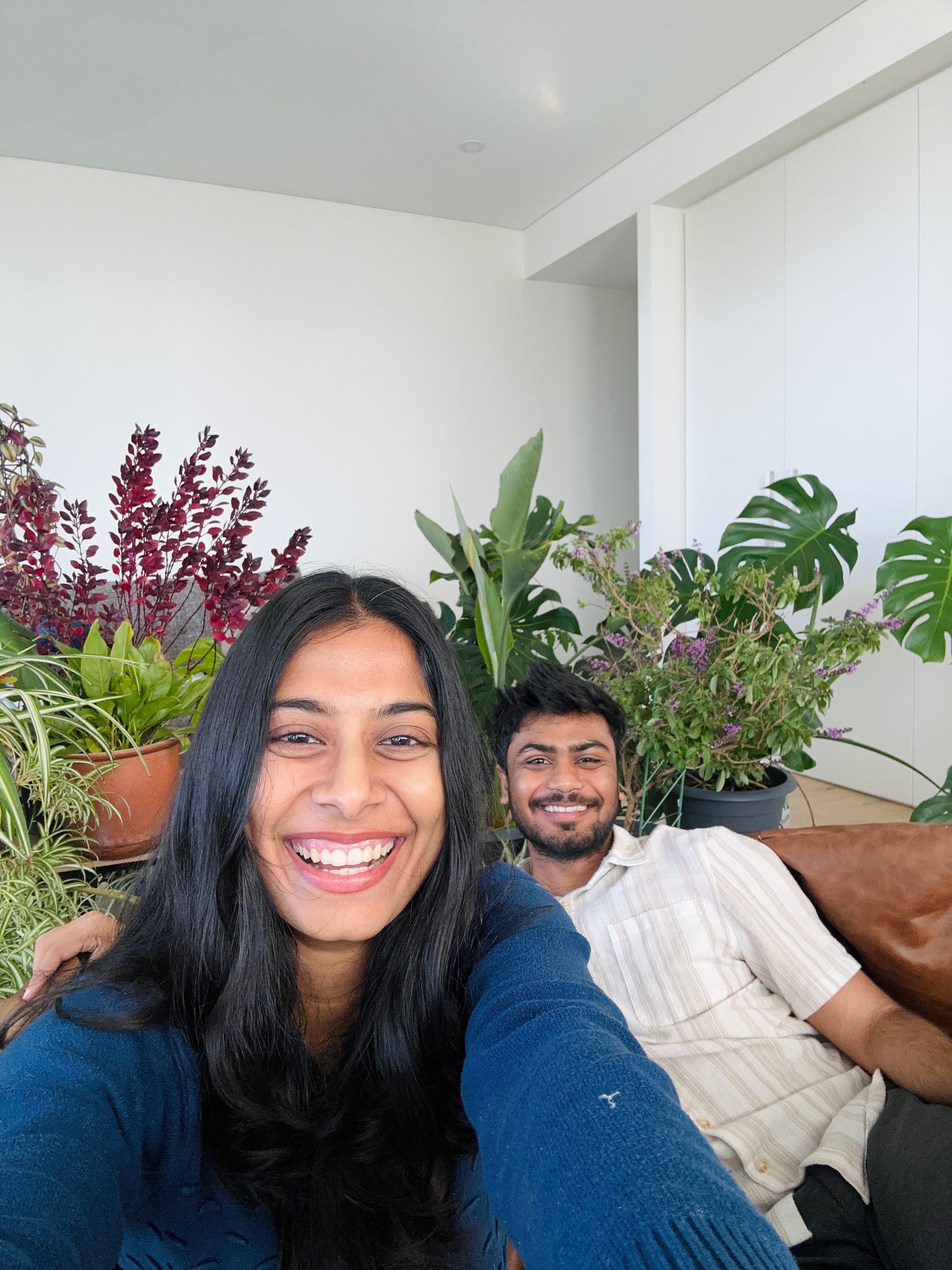 A young woman with long hair takes a selfie with a young man in the background