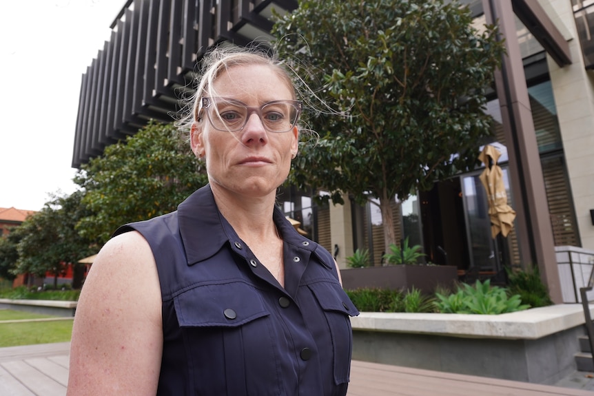 A woman in a blue sleeveless jacket looks down at a camera