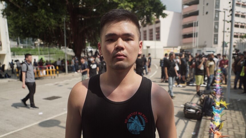A man in a black singlet looking serious while standing at a protest