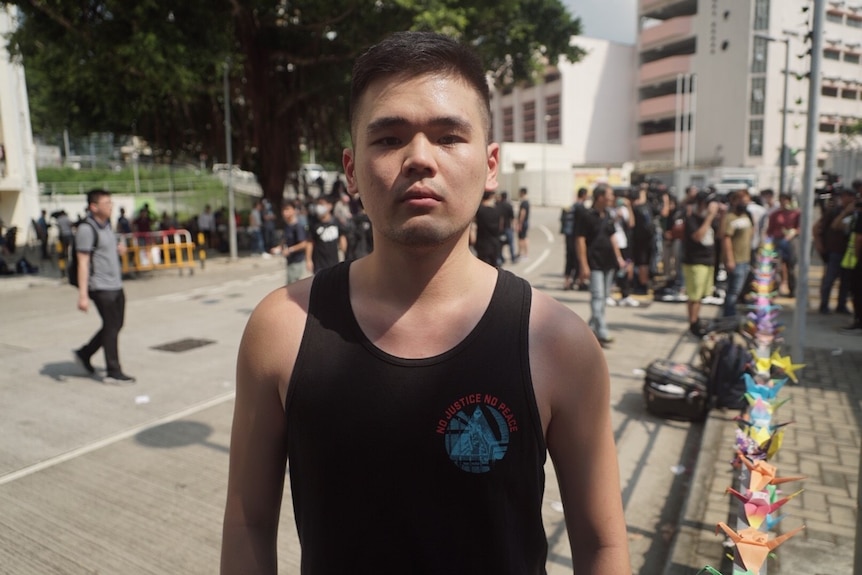 A man in a black singlet looking serious while standing at a protest