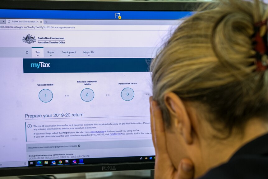 Woman with head in hands with tax return on screen in the background.