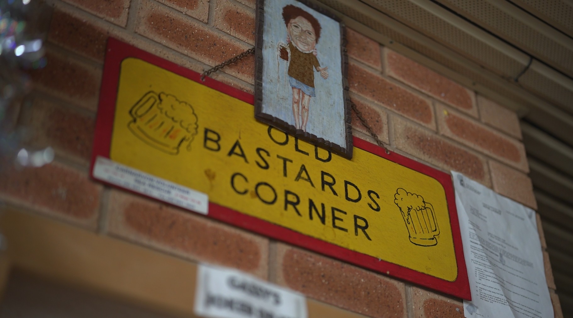 A board in a pub saying Old Bastards Corner and a photo of a deceased former member spilling her drinks.