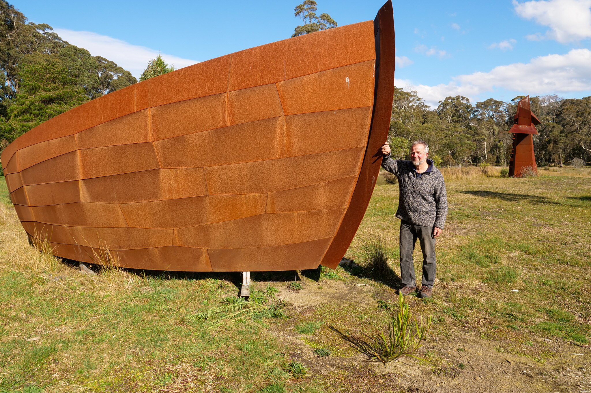 A man stands next to a giant boat-like sculpture.