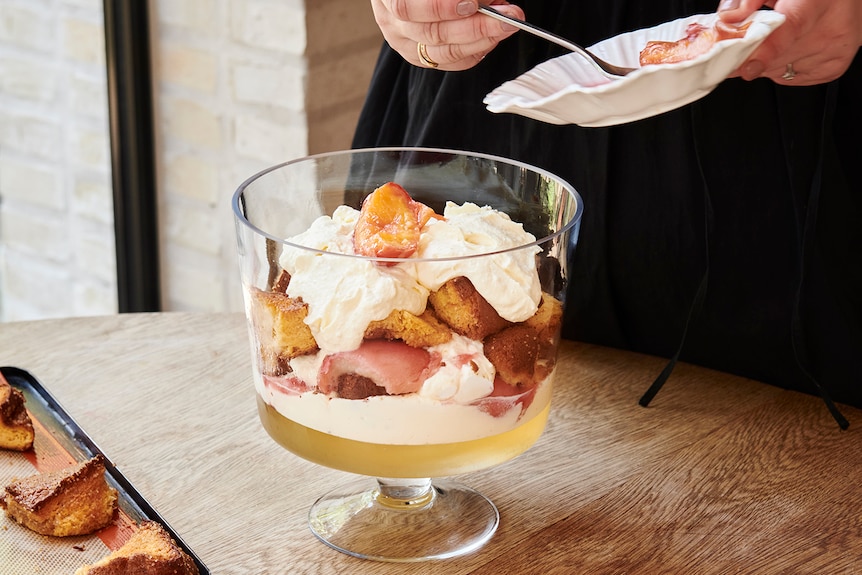 A trifle with peaches, ricotta cream and green tea jelly being assembled in a large glass bowl.