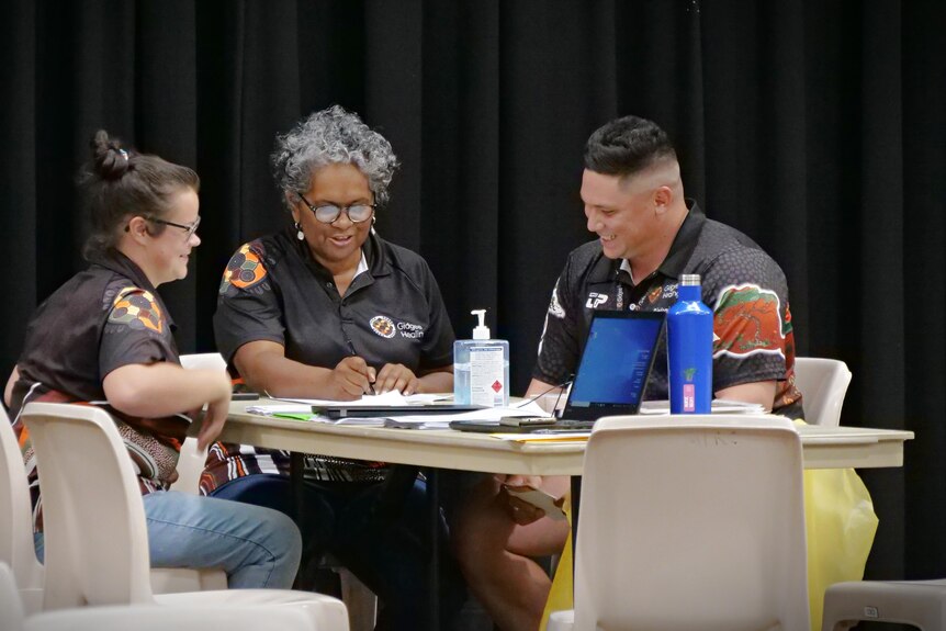 Three people sit at a table in a hall