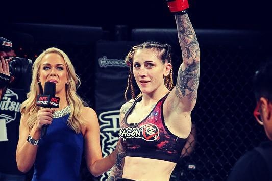 Megan Anderson wears a title belt with her gloved fist in the air in a ring to celebrate her win.