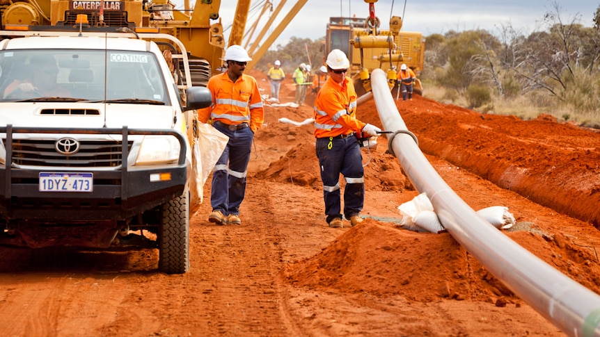 Workers lay pipeline in red dirt trenches.