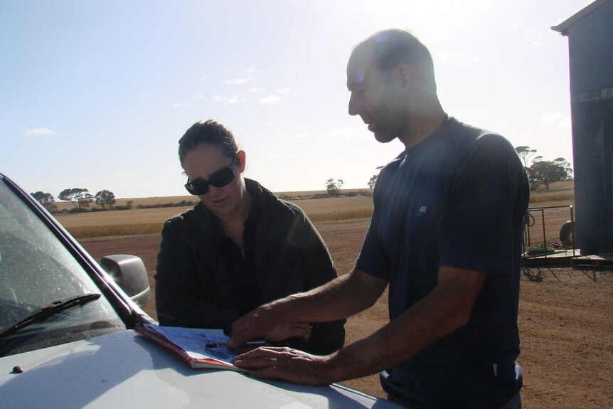 Woman and man looking at a map on car bonnet with dry farmland in background.