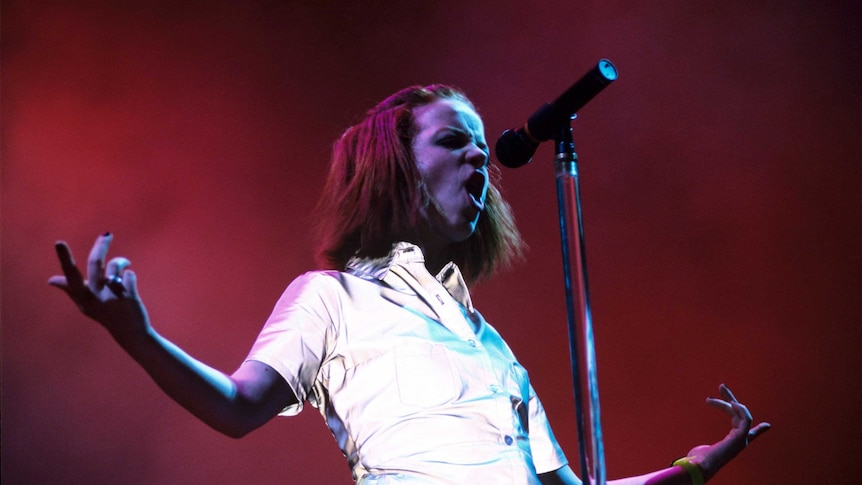 Shirley Manson of Garbage wearing a reflective jumpsuit and singing rebelliously into a microphone