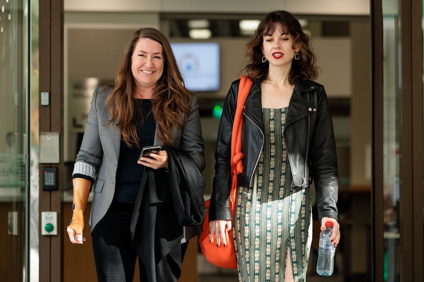 Two women walk out of a court building. One is smiling.