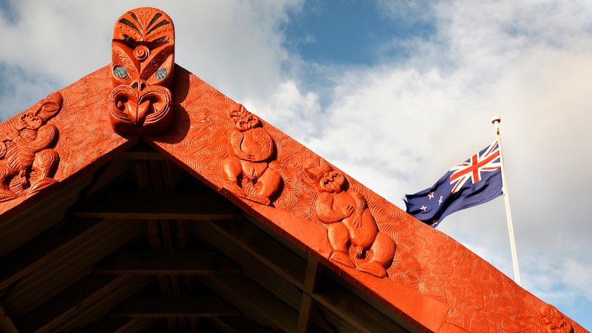 A Māori carved entrance in front of the New Zealand flag.