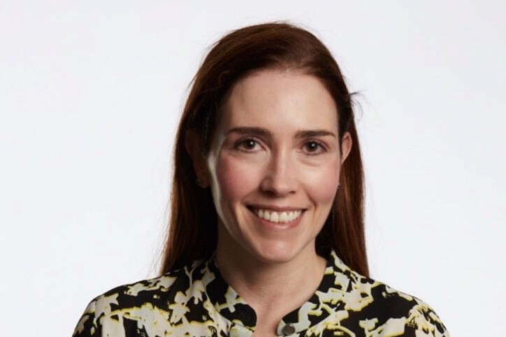 A woman smiles in front of a white background