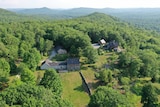 An aerial image of a house nestled among forested hills.