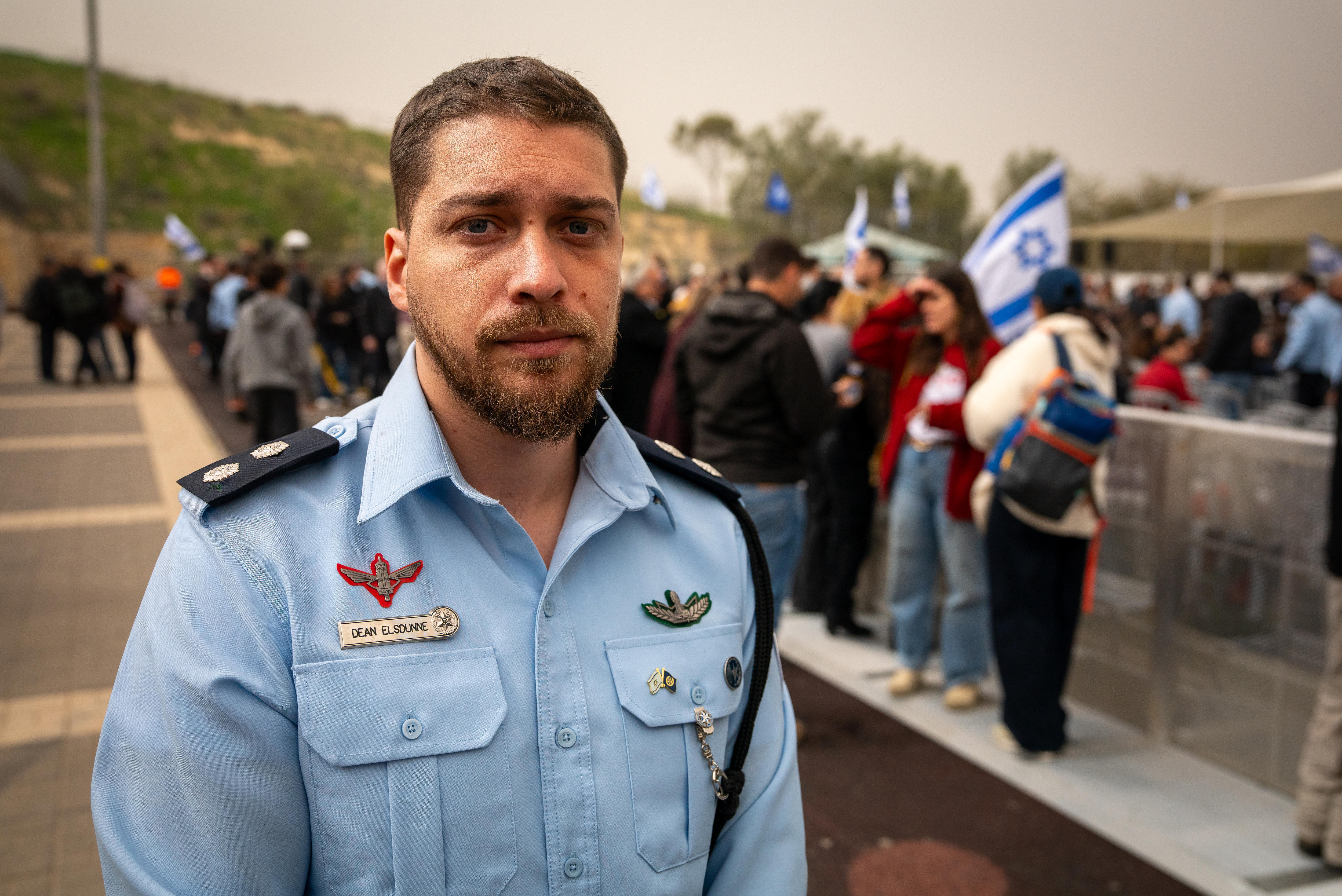 Um homem na casa dos 40 anos, com uniforme de policial, barba preta, cabelo preto curto e olhos castanhos.