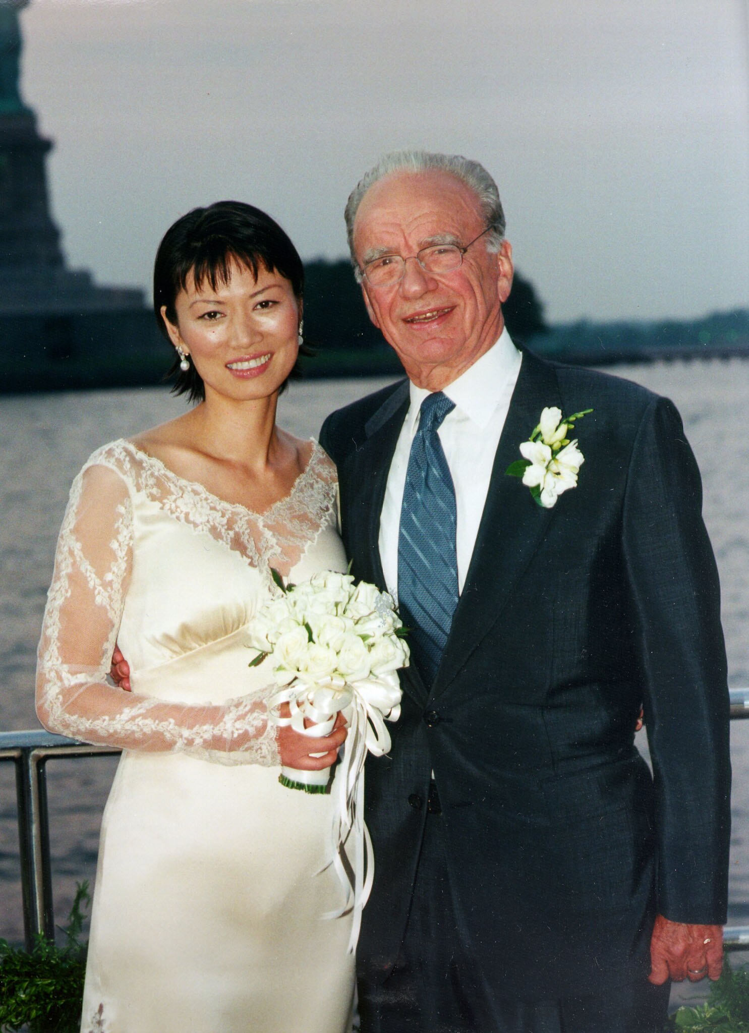 Wendi Deng in a white lace wedding dress, holding a bouquet, next to Rupert Murdoch in a suit