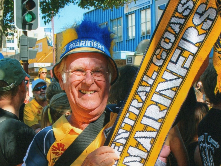 Man smiling in Mariners gear holding a scarf