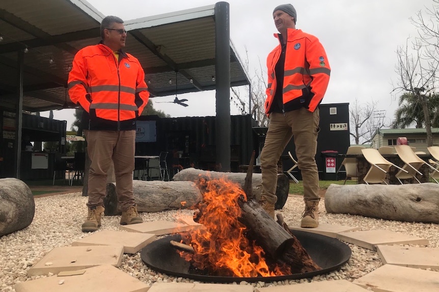Two guys in front of a fire wearing high vis.