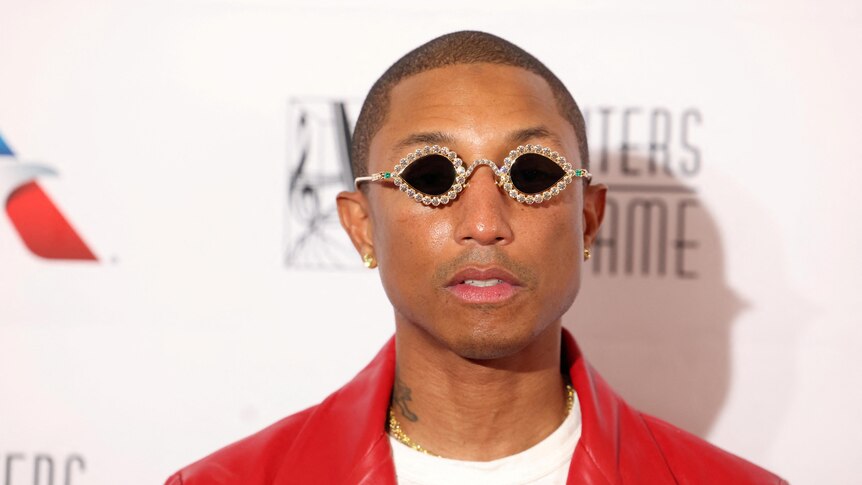 Pharrell Williams in diamond-studded glasses and a red jacket.