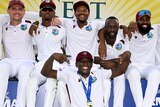 West Indies players sit together, arm in arm, with Shamar Joseph in front of them wearing a medal