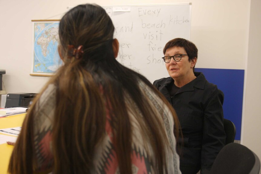 Teacher talking to student in a classroom with a whiteboard in the background.