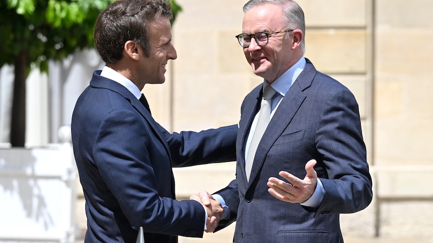 Two men, dressed in suits, greet each other and shake hands