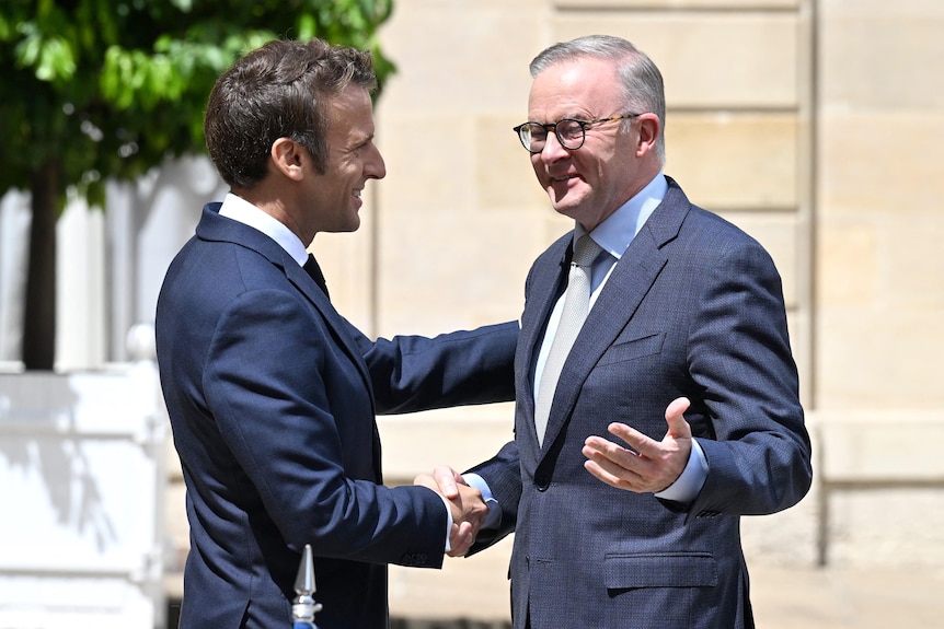 Two men, dressed in suits, greet each other and shake hands