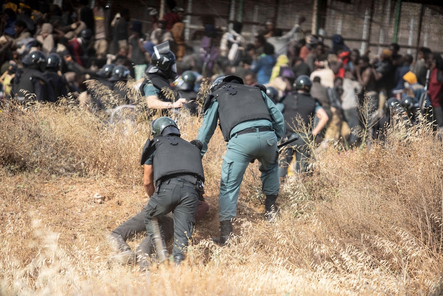 Riot police officers restrain a person on the ground