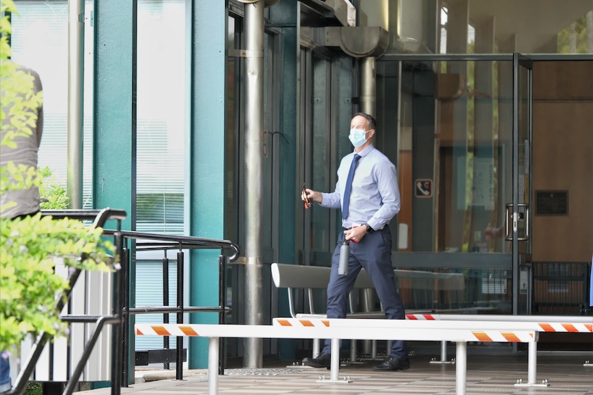 A masked man in a shirt and tie outside a court building.