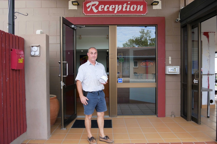 Man holds a toilet roll outside of his motel which reads reception