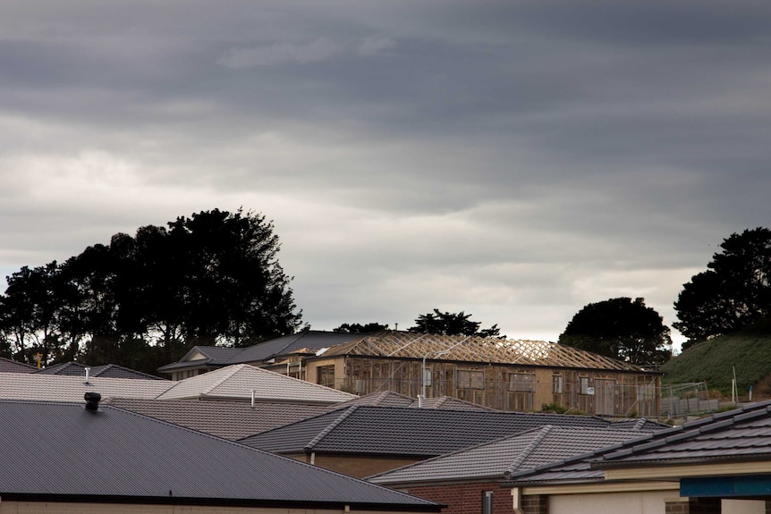 Suburban roofs, house under construction in background.