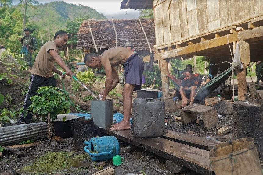 A man holds a hose while another washes his hands as others watch on near their house.
