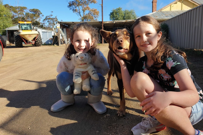 Two kids sit on ground with dog