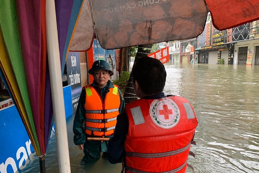 Two people stand in knee-length flood water in Vietnam.