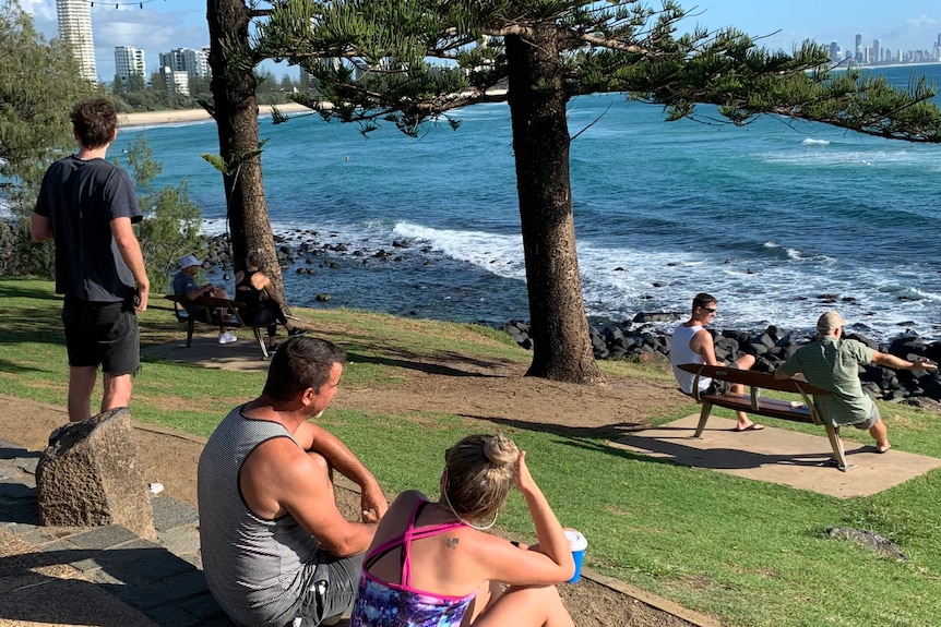 people sitting on a grassy area near a beach