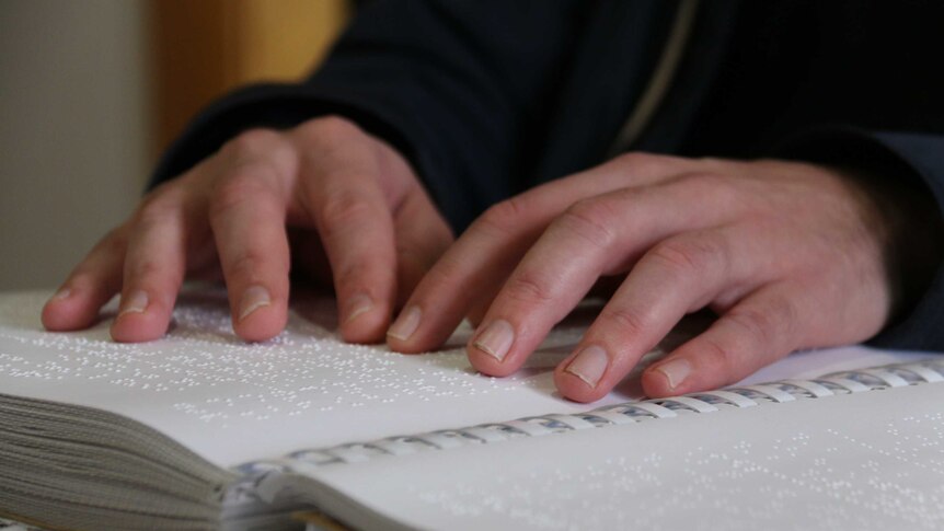 A close-up image of fingers reading a book in Braille.