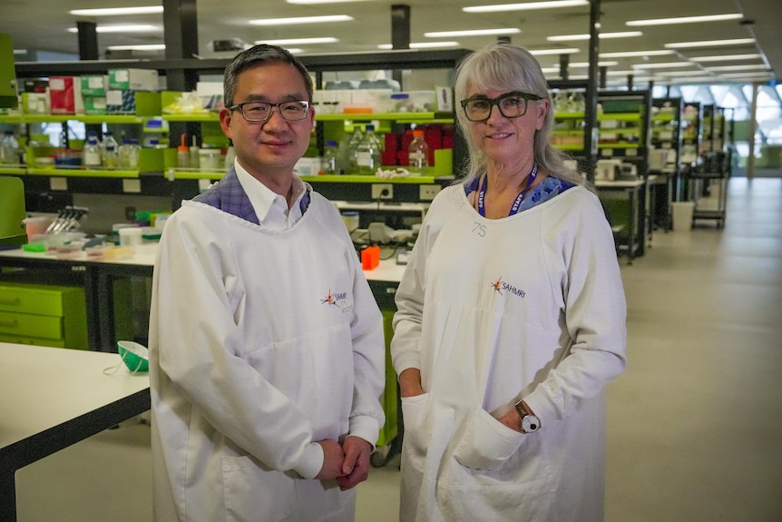 A man and a woman with lab coats over their civvies pose in a lab