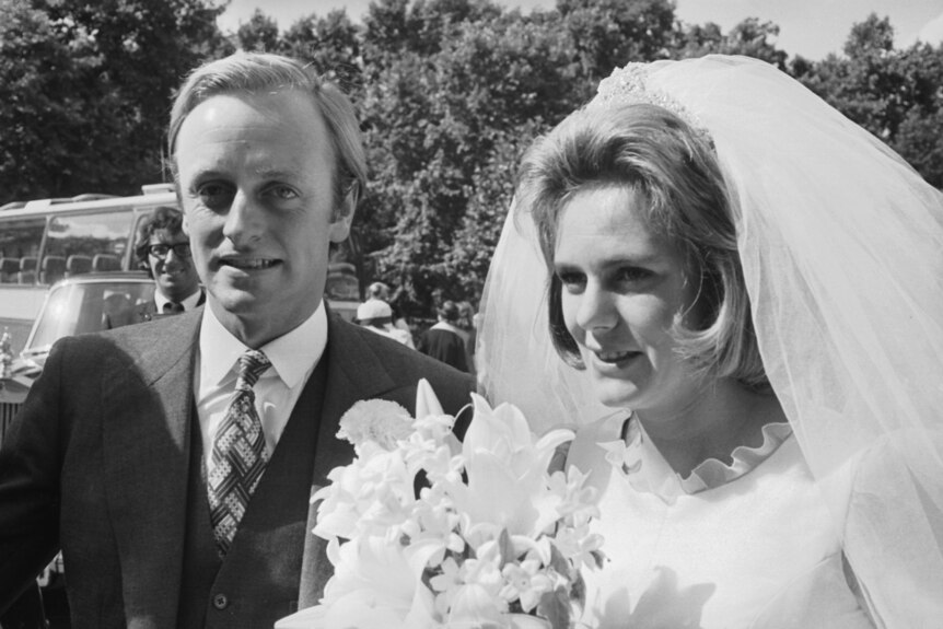 A black and white close up of a man wearing a formal suit and a woman wearing a veil and wedding dress.