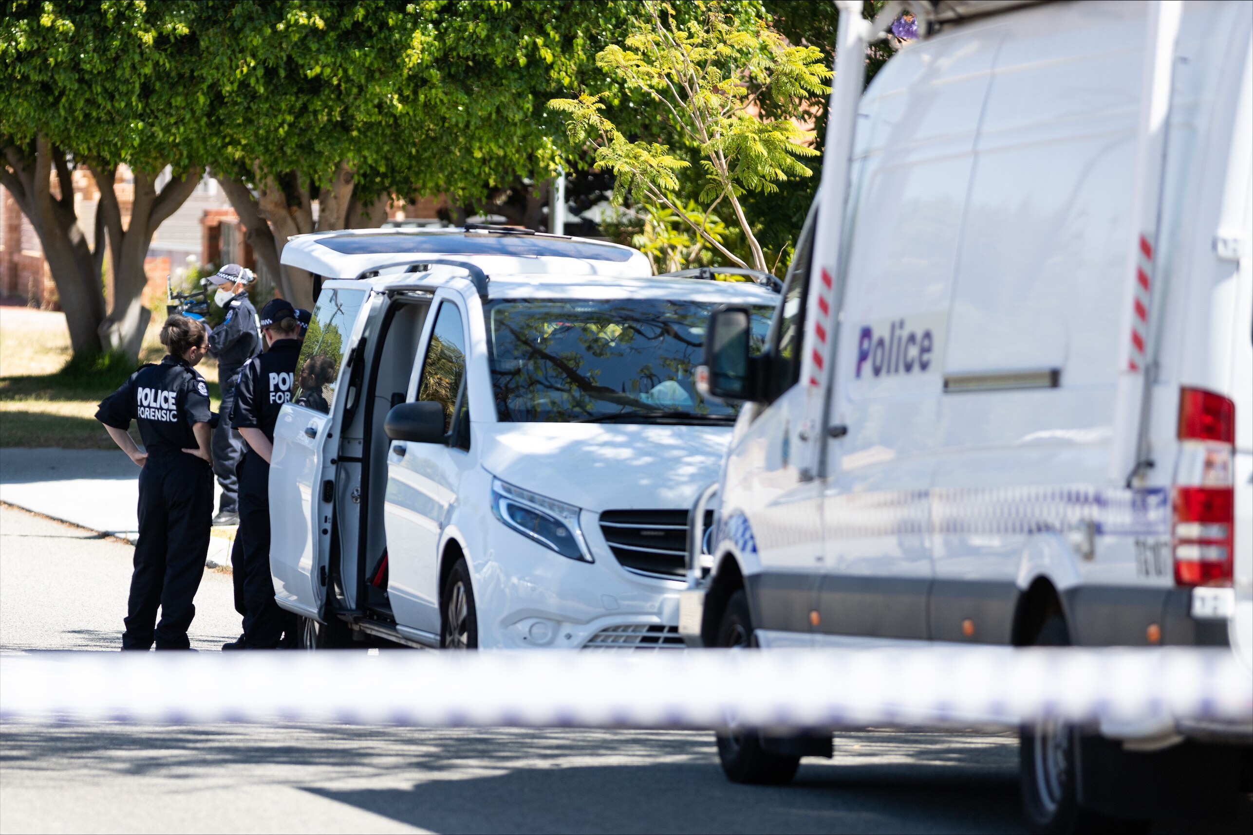 Police forensic officers standing next to white vehicles. 