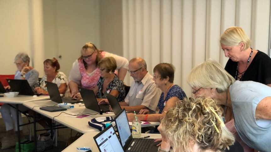 A group of older Australians in a workshop with laptops and mentors.