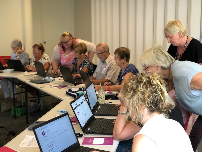 A group of older Australians in a workshop with laptops and mentors.